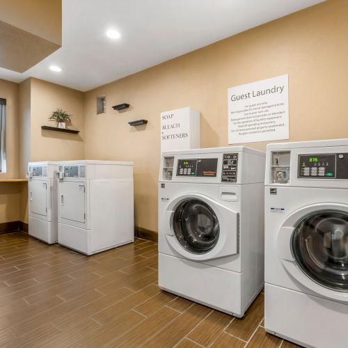 A modern laundry room with washers and dryers, a folding table by the window, and a sign reading 