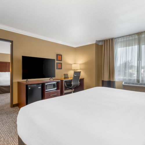 A hotel room with a bed, desk, TV, and a view of a connected room with another bed.