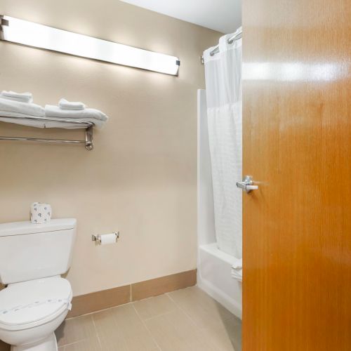 A clean bathroom featuring a toilet, a bathtub with a shower curtain, a towel rack with folded towels, and a wooden door, all in neutral tones.