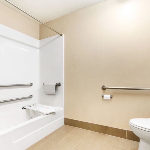 This image shows a clean bathroom featuring a shower with grab bars, a toilet with a rail, and a towel hanging on a holder.