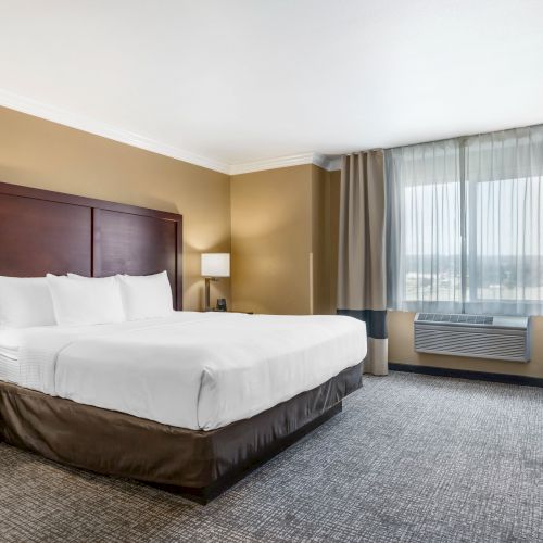 This image shows a hotel room with a large double bed, two bedside tables with lamps, a window with curtains, and a desk with a chair.