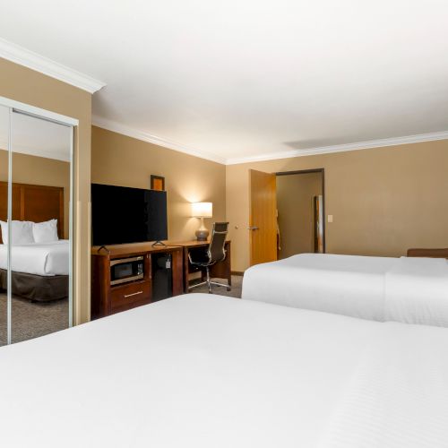 A hotel room with two beds, a mirror, a TV on a wooden stand, a desk with a chair, and bedside lamps on either side of the beds.