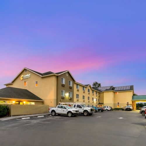 The image shows a hotel building with parked cars in front, taken during sunset under a colorful sky.