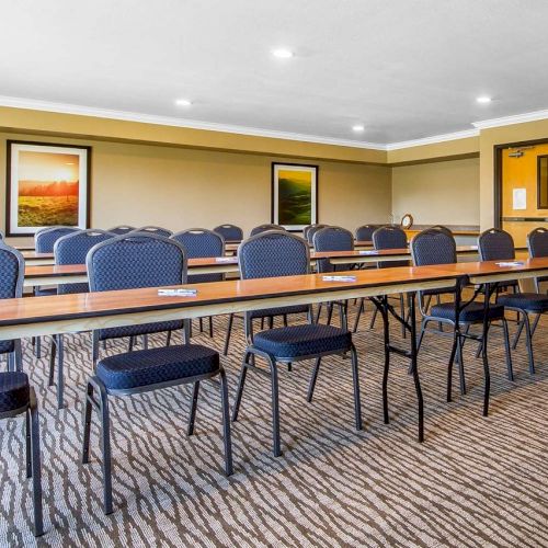 An empty conference room with rows of tables and chairs, beige walls, framed artwork, and double doors at the back.