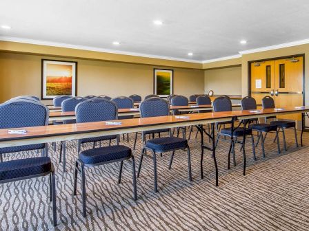 A conference room setup with rows of tables and chairs facing a door, adorned with framed landscape pictures in the background.