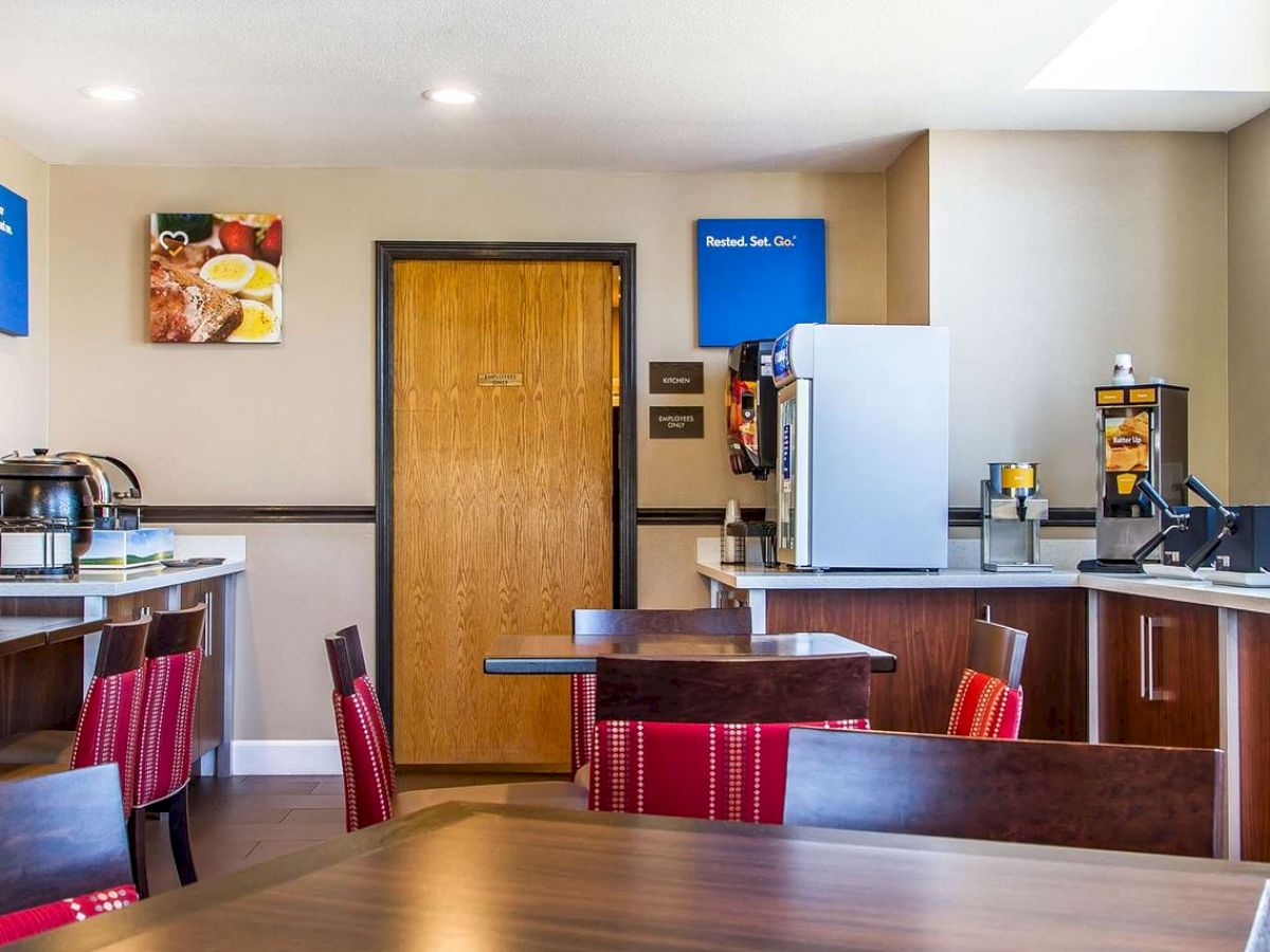 The image shows a small breakfast area with seating, a beverage station, and food counter, all set with wooden furniture and red cushioned chairs.